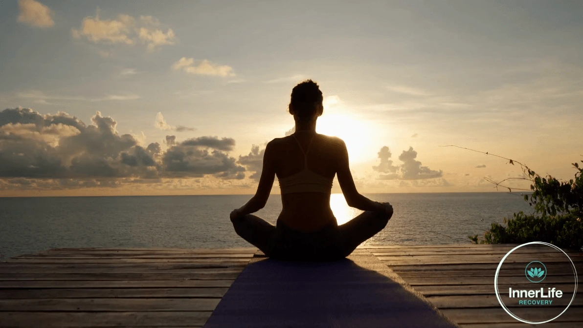 Woman meditating with beautiful sunset with InnerLife Recovery rehab in Spain logo